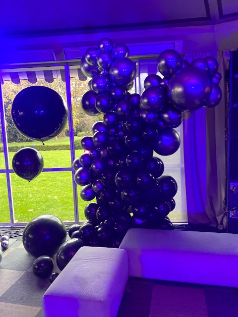 Zdjęcie z balonową instalacją w czarno-srebrno-fioletowych barwach, umieszczoną przy oknach restauracji Belvedere z widokiem na naturę. Oświetlenie podkreśla stylową atmosferę wnętrza