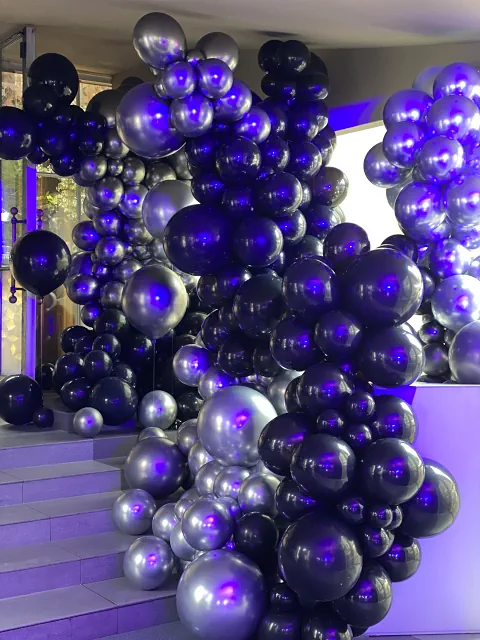 Dekoracja z balonów w czerni, srebrze i fiolecie, umieszczona w sali restauracji Belvedere z oknami na ogród. Nowoczesne oświetlenie i meble dodają wnętrzu luksusowego charakteru