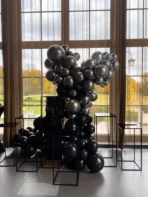 Elegancka aranżacja balonowa w kolorach czerni, srebra i fioletu, zdobiąca wnętrze z dużymi oknami i widokiem na jesienny krajobraz. Oświetlenie nadaje magiczny nastrój sali restauracji Belvedere