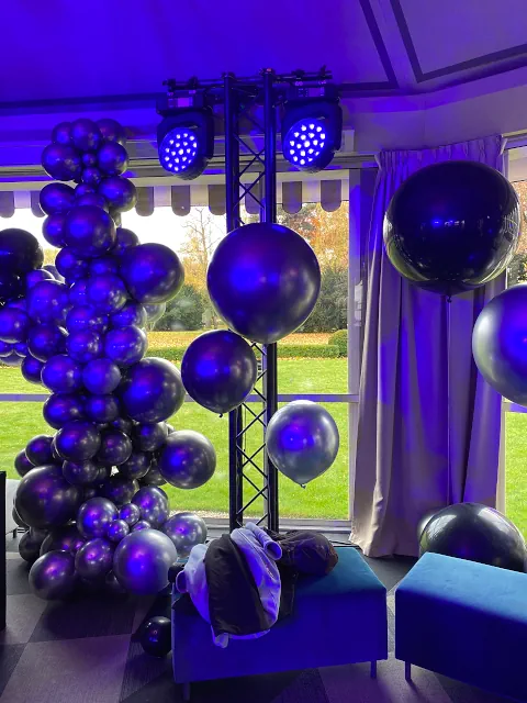 Zdjęcie z dekoracją balonową w odcieniach czerni, srebra i fioletu, ustawioną przy oknie z widokiem na ogród. Balony tworzą efektowną instalację, a oświetlenie podkreśla elegancję wnętrza restauracji Belvedere Warszawa
