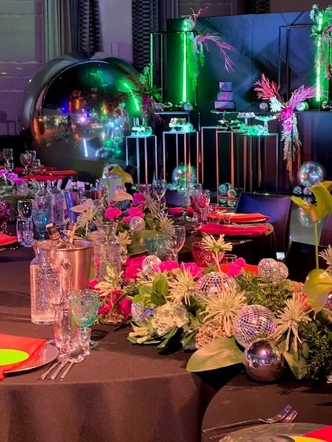 W Hotelu Rubin koło Radomia, elegancka dekoracja stołu z kolorowymi kwiatami, lustrzanymi kulami, neonowymi akcentami i szkłem, tworzącymi luksusową atmosferę