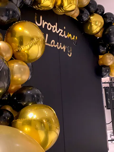 Starannie wykonana dekoracja urodzinowa w Warszawie, elegancki łuk z błyszczących balonów w kolorach złotym i czarnym z centralnym napisem Urodziny Laury