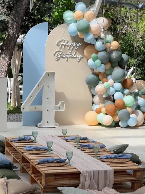 Dekoracja urodzinowa w Warszawie: pastelowa ścianka z Happy Birthday i cyfrą 4, balony, stoły z palet, piknikowy wystrój, ogród w tle