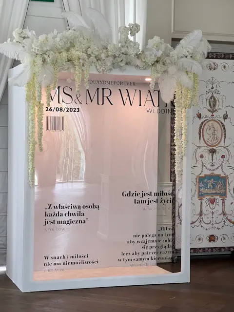 Dekoracja stołu w ogrodzie Pałacu Mała Wieś z białymi kwiatami, świecami w latarniach, kieliszkami i chłodzoną wodą, otoczonego bujnymi aranżacjami kwiatowymi